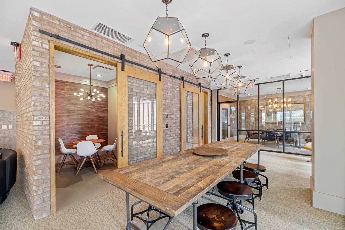 Placemakr Premier SoBro lounge with a long wooden gathering table, brick walls and glass-front meeting rooms
