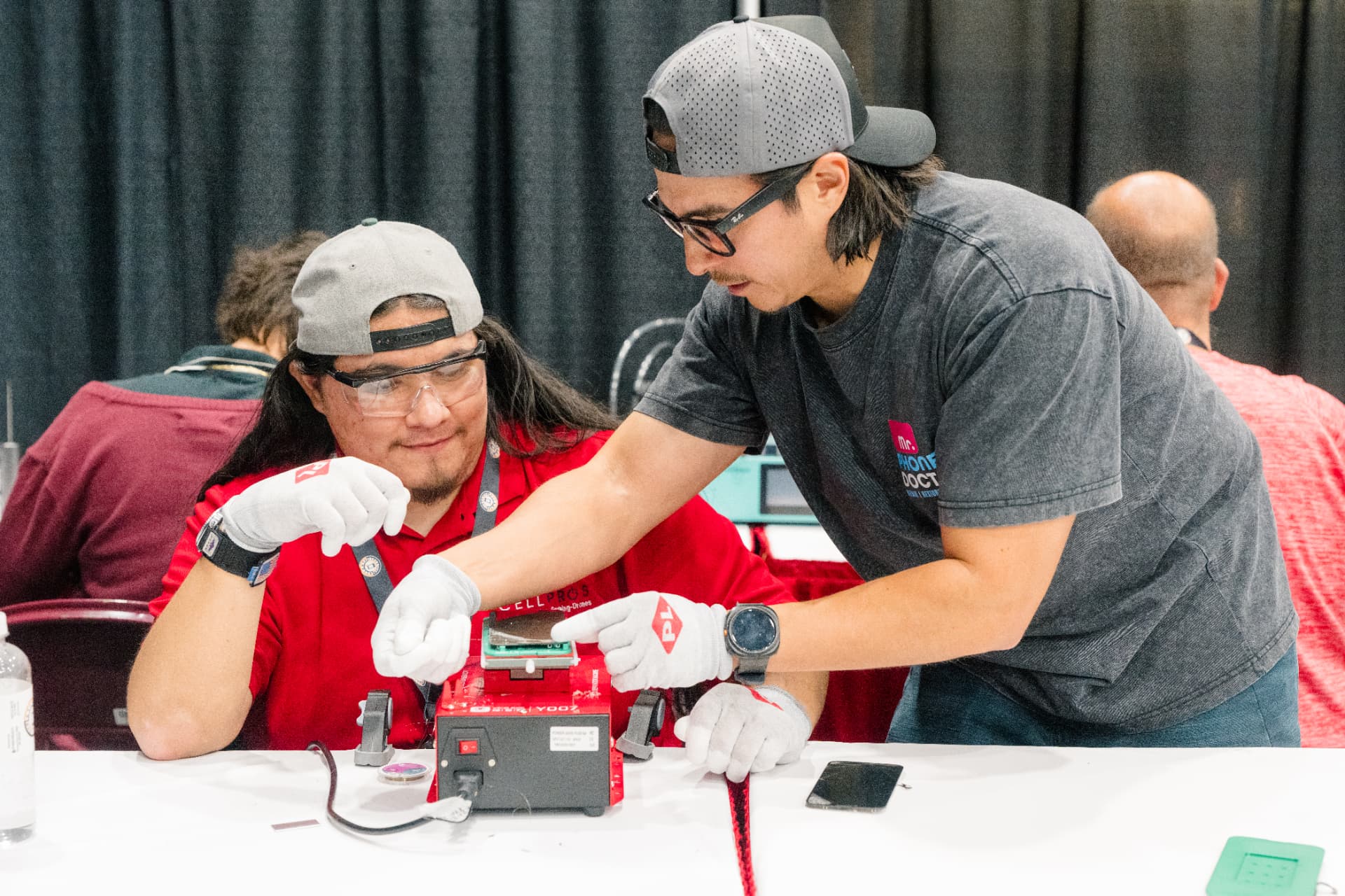 Two technicians working on a device at a live repair demo bench