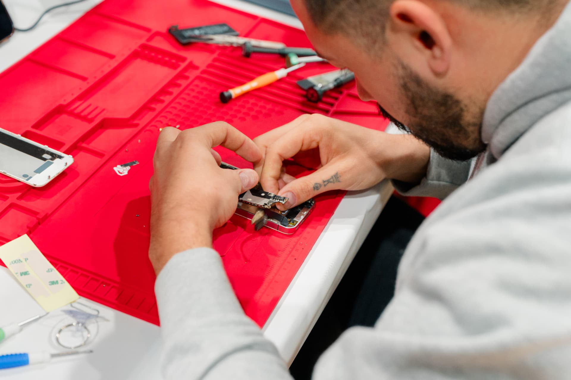 Close-up of a technician reassembling a phone display on a red repair mat
